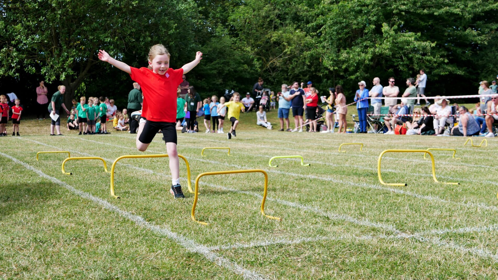 physical education with a girl jumping over hurdles at sports day